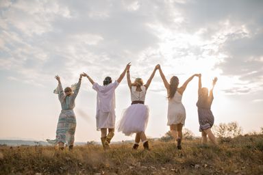 Fünf Frauen laufen, Hand haltend in wehenden Hippie-Kleidern in Richtung Sonnenuntergang