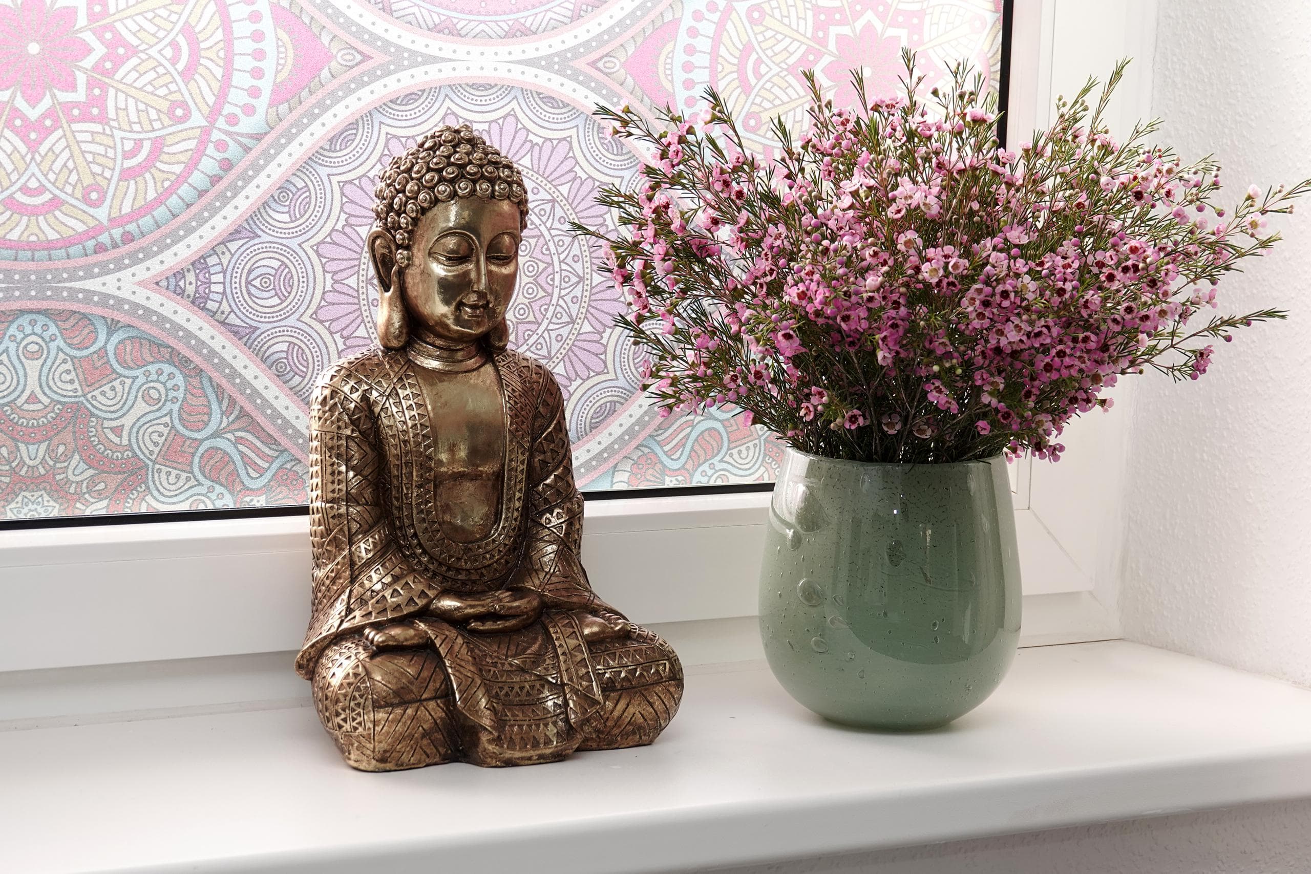 Buddha und Blumenstrauß vor bunter Fensterfolie im Yogahäuschen.